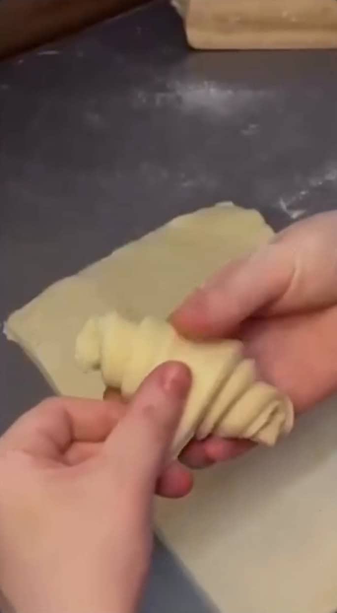 Mãos enrolando um croissant cru sobre a bancada.